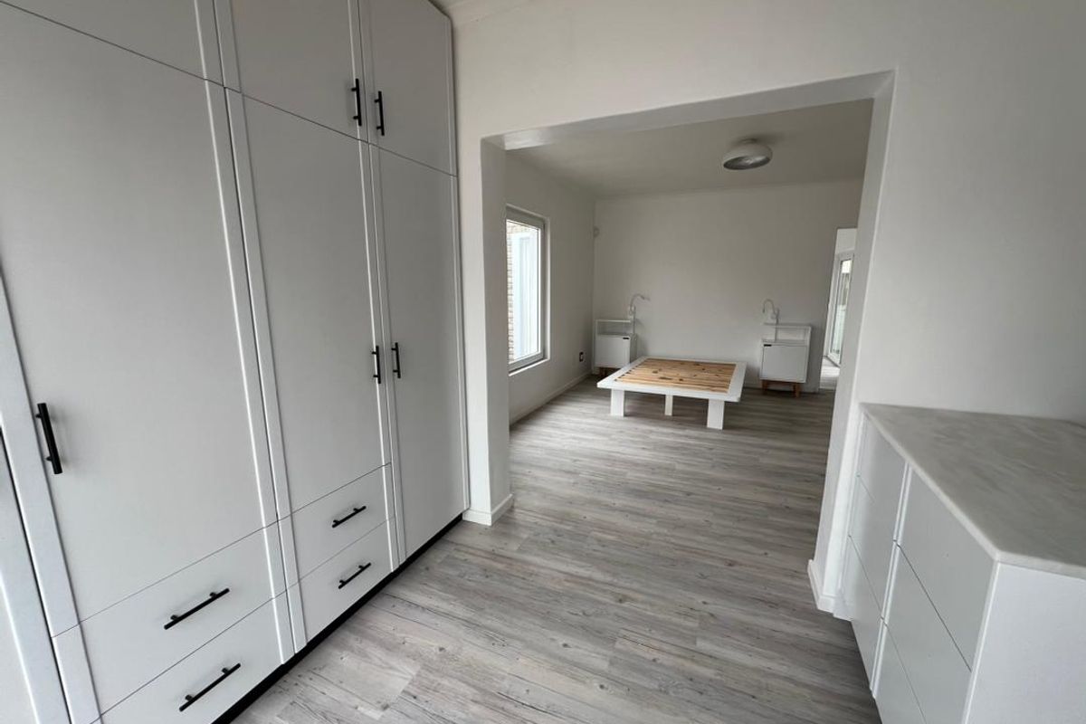 A bright bedroom featuring extensive built-in cabinetry, light wood-look flooring, and a spacious layout with an adjoining area.