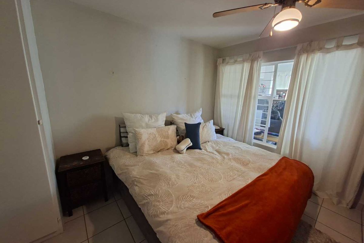 A functional bedroom featuring tiled flooring, a ceiling fan, and a built-in wardrobe, offering a comfortable and practical living space.