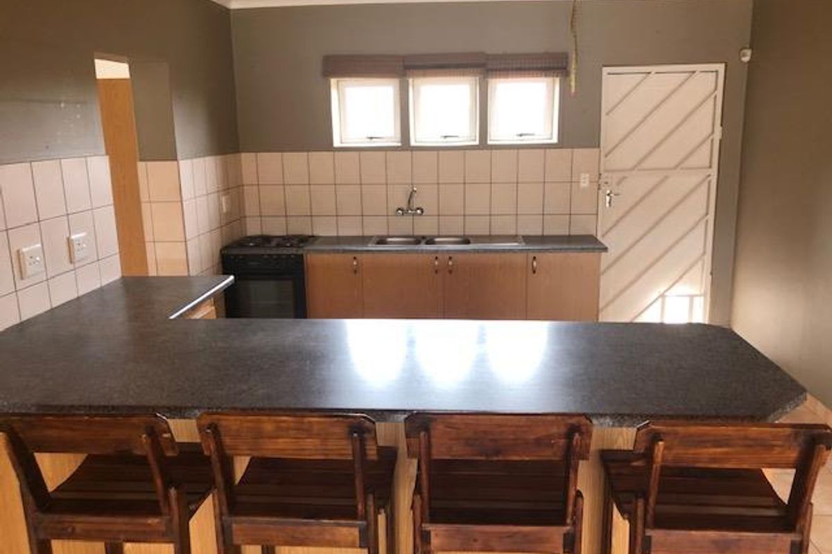 A functional kitchen featuring a breakfast bar, built-in cabinetry, a double sink, and a stove, with a neutral color palette and tiled splashback.