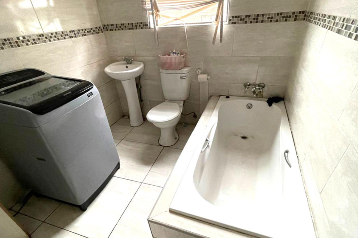A functional bathroom featuring a built-in bathtub, pedestal basin, and toilet, with tiled walls and flooring throughout.