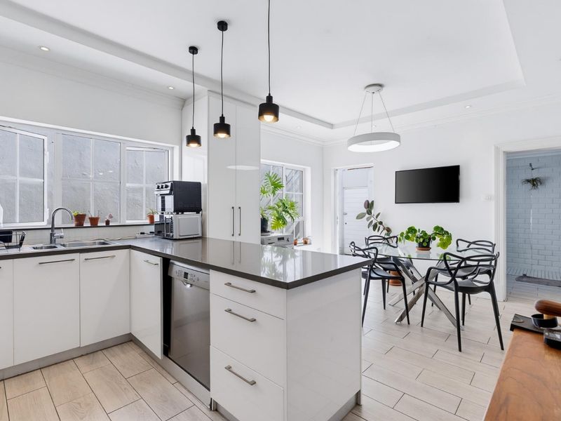 Modern open-plan kitchen and dining area featuring sleek white cabinetry, stone countertops, integrated appliances, and contemporary pendant lighting.