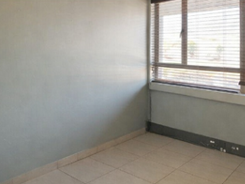 A vacant office space featuring neutral tiled flooring, large windows with fitted venetian blinds, and plain painted walls.