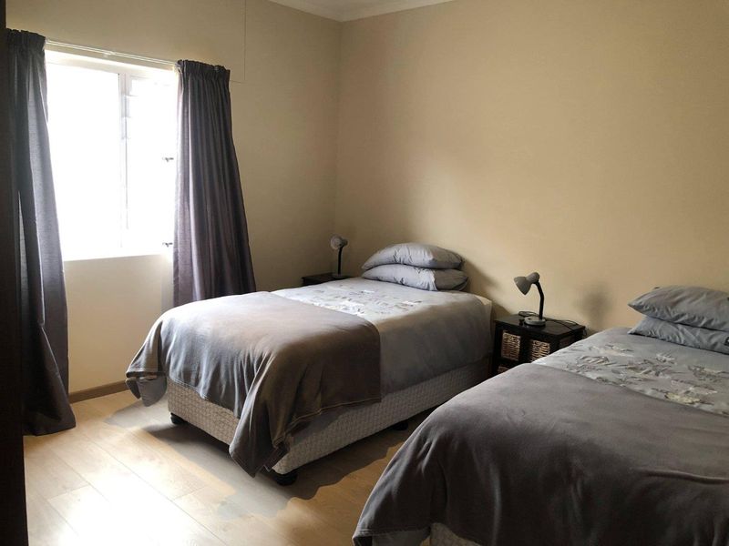 A functional bedroom featuring light-toned laminate flooring and a window with curtains, providing a neutral base for interior design updates.