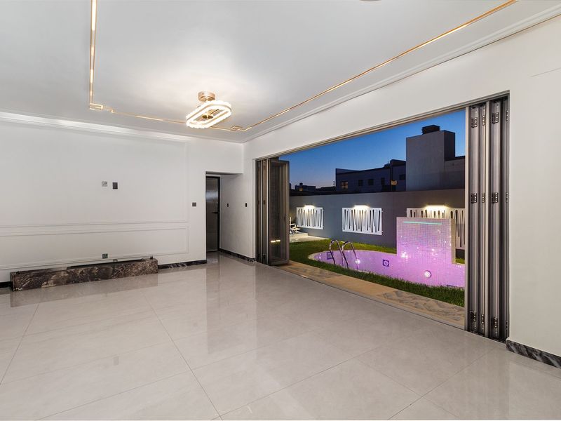 Spacious living area featuring large bi-fold doors opening to a private pool area, elegant wall molding, and polished tiled flooring.