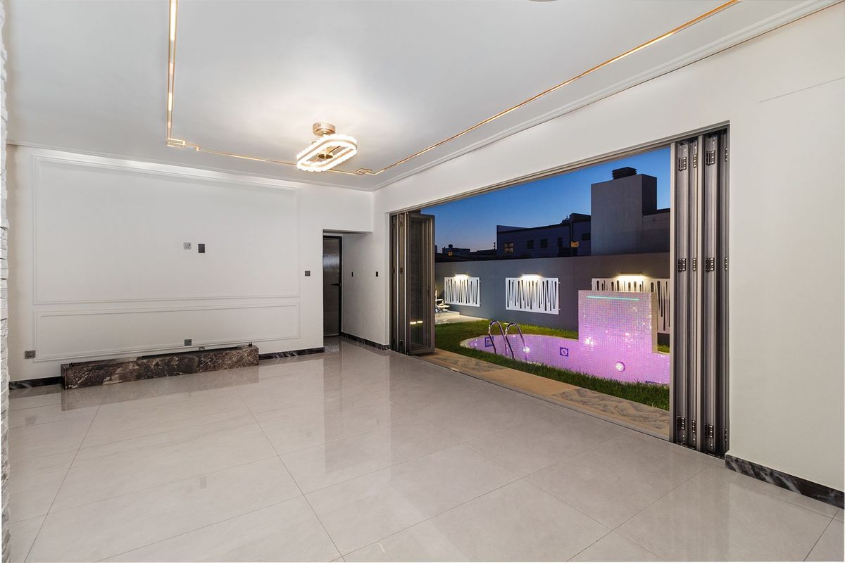 Spacious living area featuring large bi-fold doors opening to a private pool area, elegant wall molding, and polished tiled flooring.