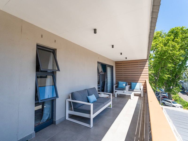 A modern, covered balcony featuring tiled flooring, recessed lighting, and a sleek metal balustrade, offering a pleasant outdoor space.