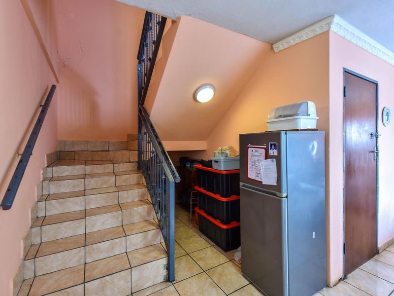 A functional hallway area featuring a tiled staircase with a wrought iron balustrade and wall-mounted handrail, leading to the upper level of the townhouse.