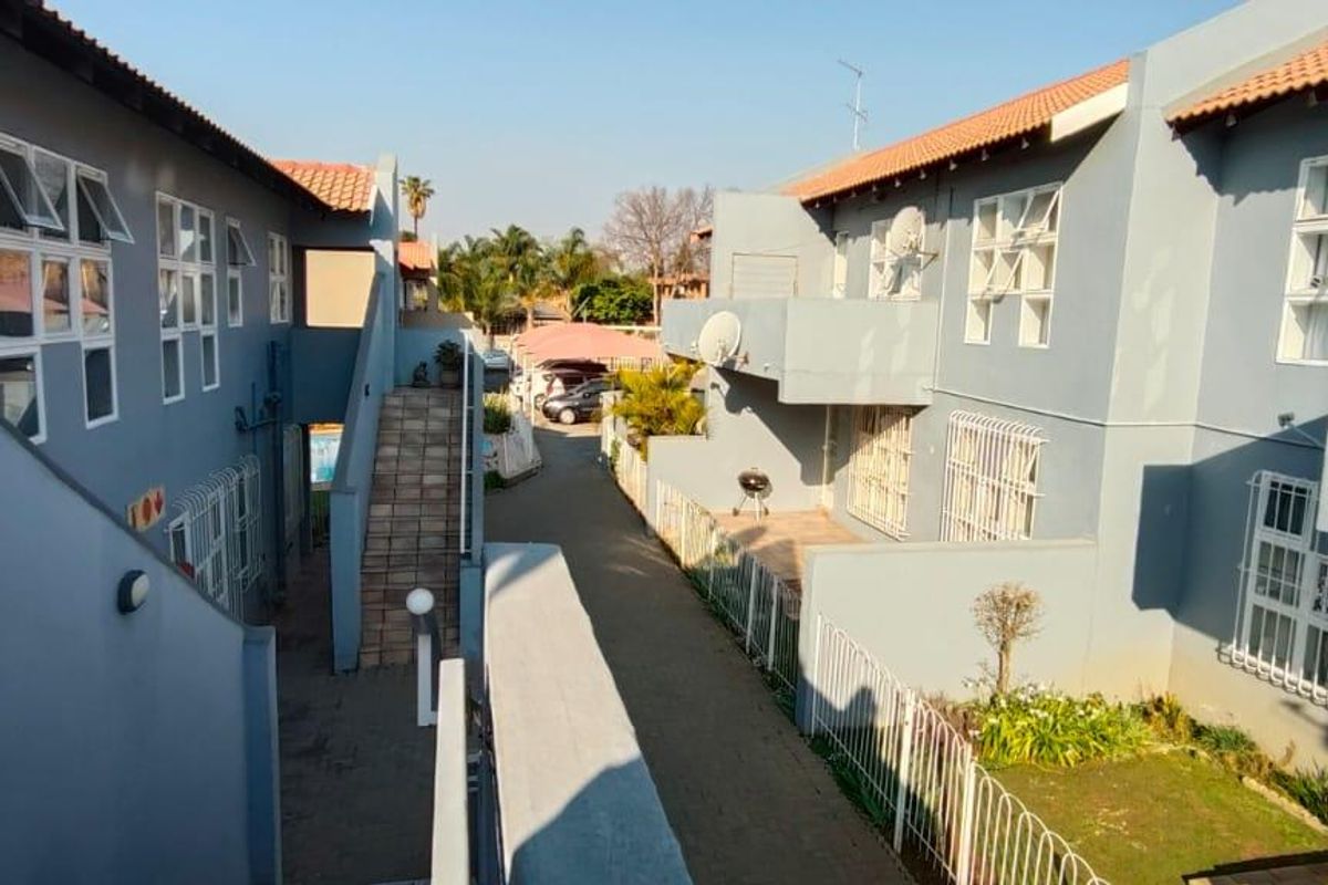 Exterior view of an apartment complex featuring multi-level units with balconies, tiled roofs, and a central paved walkway.