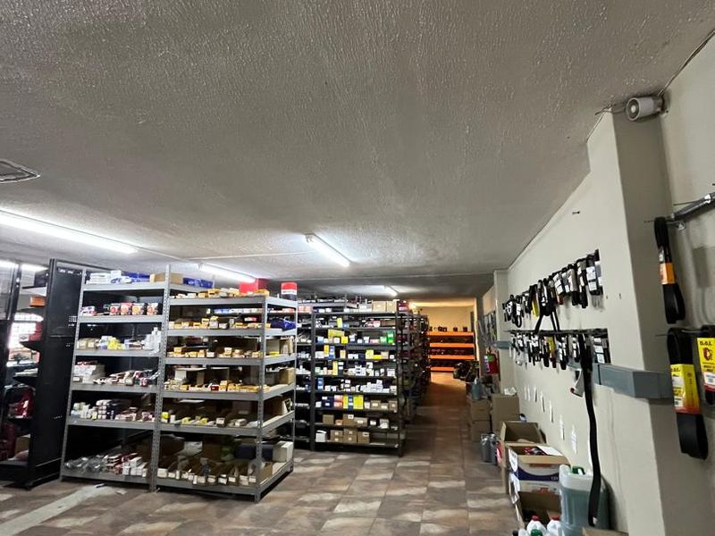 A functional utility or storage space featuring tiled flooring, textured ceilings, and overhead fluorescent lighting, currently utilized for inventory organization.
