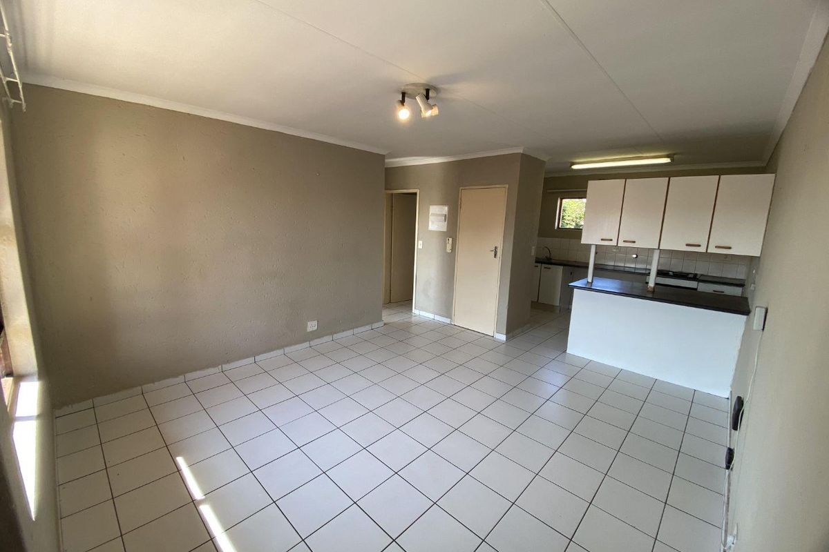 An open-plan living and kitchen area featuring tiled flooring, neutral wall tones, and functional built-in kitchen cabinetry with a breakfast counter.