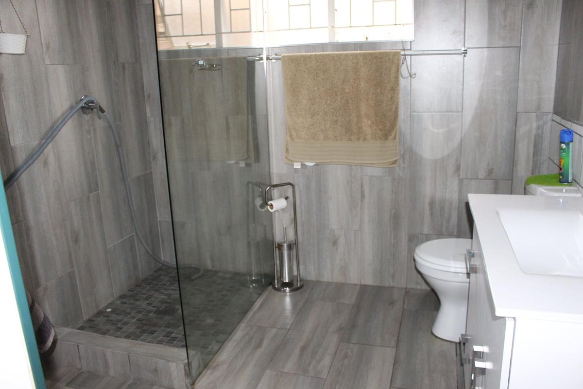 Modern bathroom featuring a walk-in shower with glass enclosure, grey wood-look floor and wall tiles, and a white vanity basin.