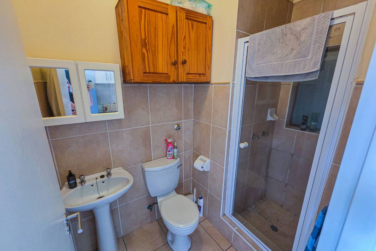 A functional bathroom featuring a pedestal basin, a standard toilet, and a glass-enclosed shower with neutral wall and floor tiling.