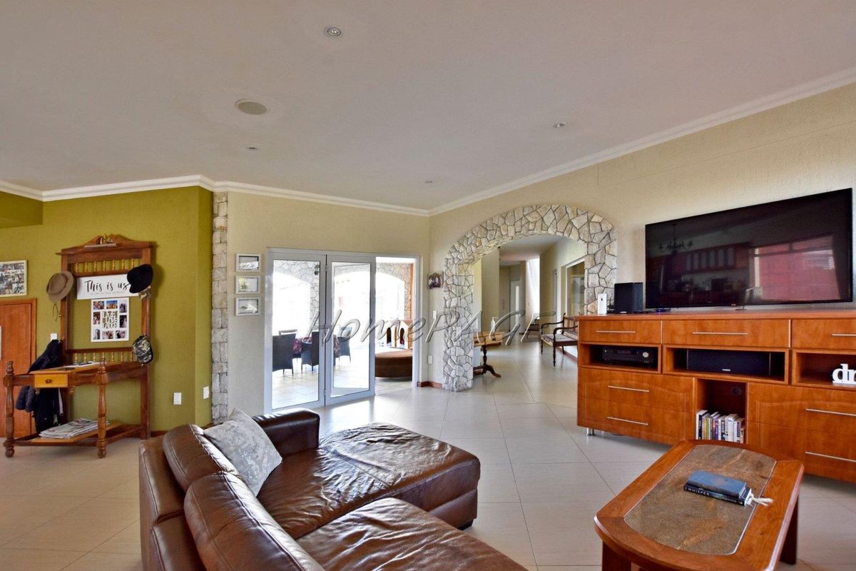 Spacious living area featuring tiled flooring, recessed ceiling lighting, and a distinctive stone-clad archway leading to the hallway and patio.