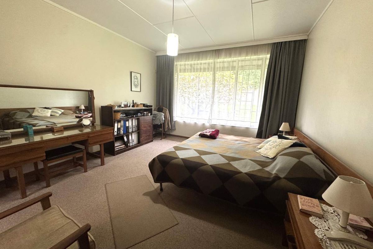 A spacious bedroom featuring large windows with curtains, neutral wall finishes, and carpeted flooring.