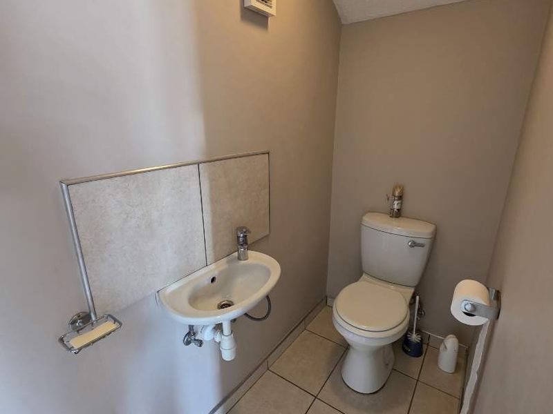 A compact guest bathroom featuring a wall-mounted basin, toilet, and tiled flooring, requiring minor cosmetic repairs to the wall surface.
