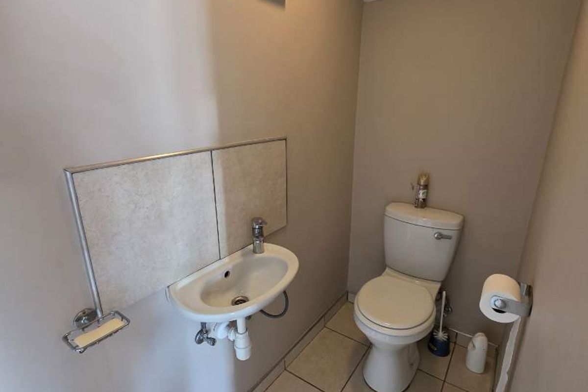 A compact guest bathroom featuring a wall-mounted basin, toilet, and tiled flooring, requiring minor cosmetic repairs to the wall surface.