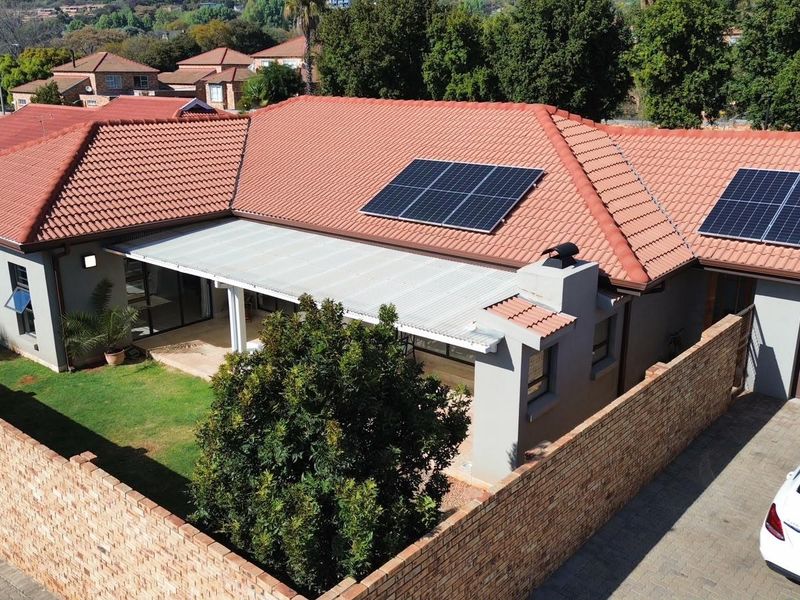 Aerial view of a cluster home featuring a tiled roof with installed solar panels, a covered patio, and a private brick-walled garden area.
