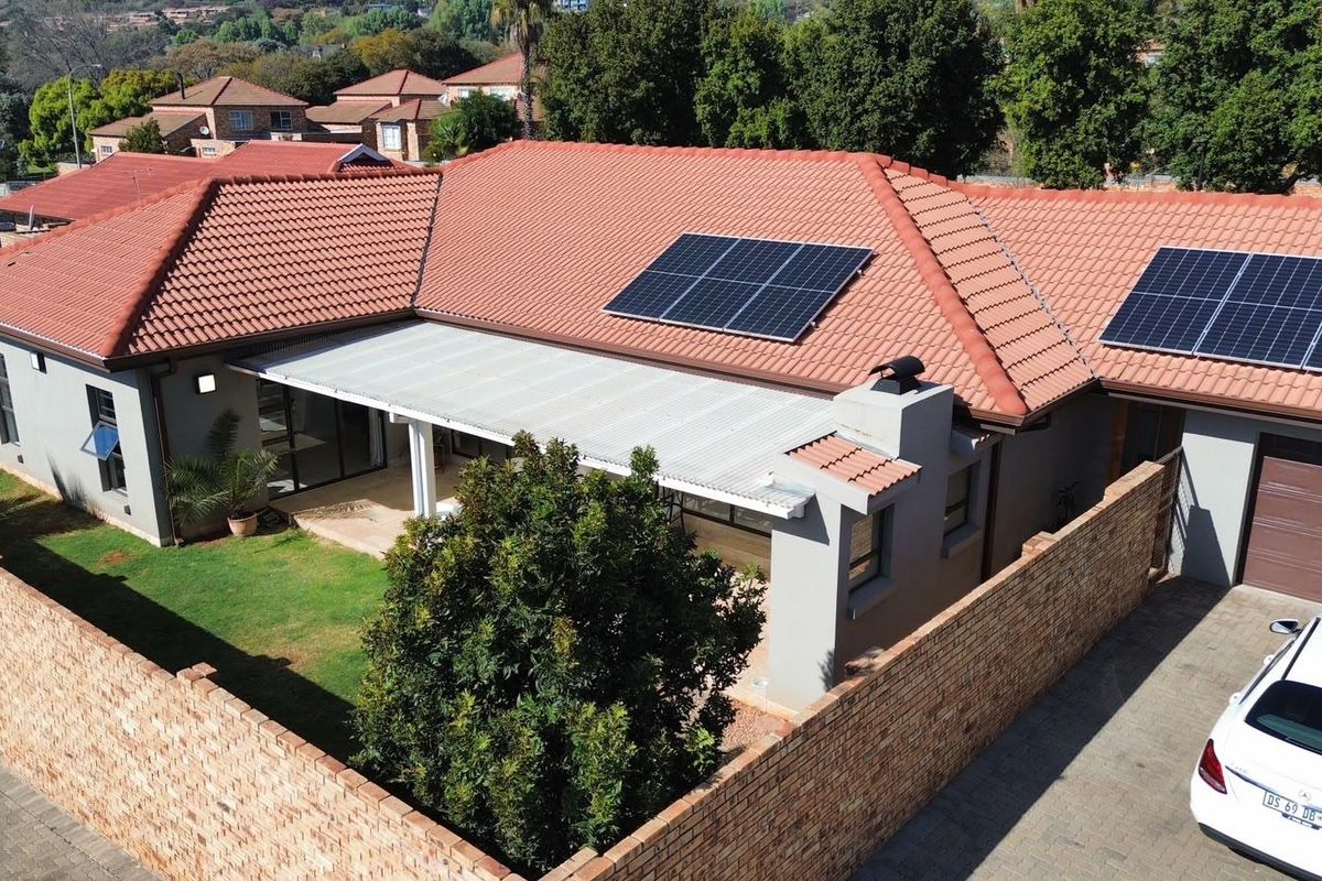 Aerial view of a cluster home featuring a tiled roof with installed solar panels, a covered patio, and a private brick-walled garden area.