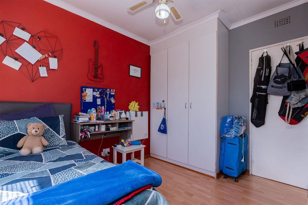 A bedroom featuring laminate flooring, a built-in wardrobe, and a ceiling fan, with a bold red accent wall.