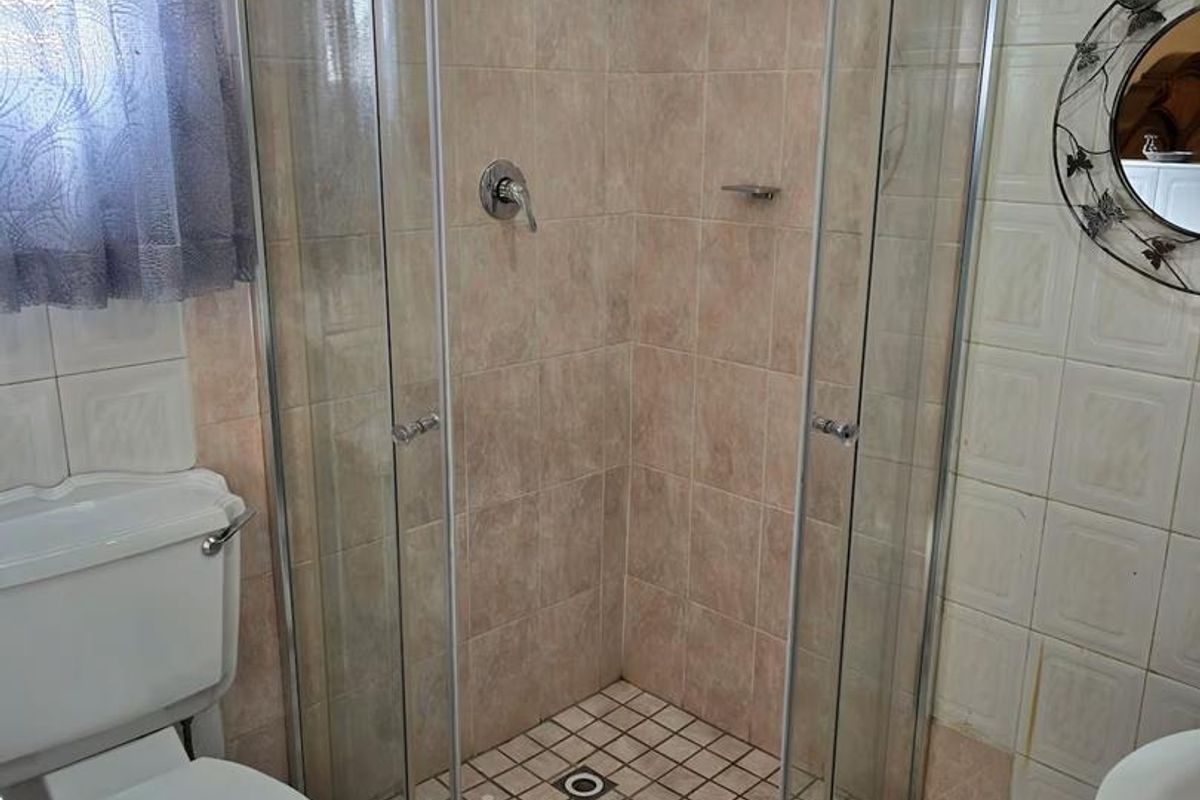 A functional bathroom featuring a corner glass shower enclosure, a standard toilet, and tiled wall and floor finishes.