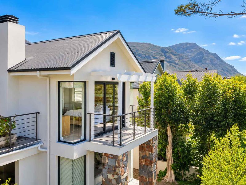 A well-maintained rear exterior view featuring a modern balcony, stone cladding, and a metal roof set against a scenic mountain backdrop.