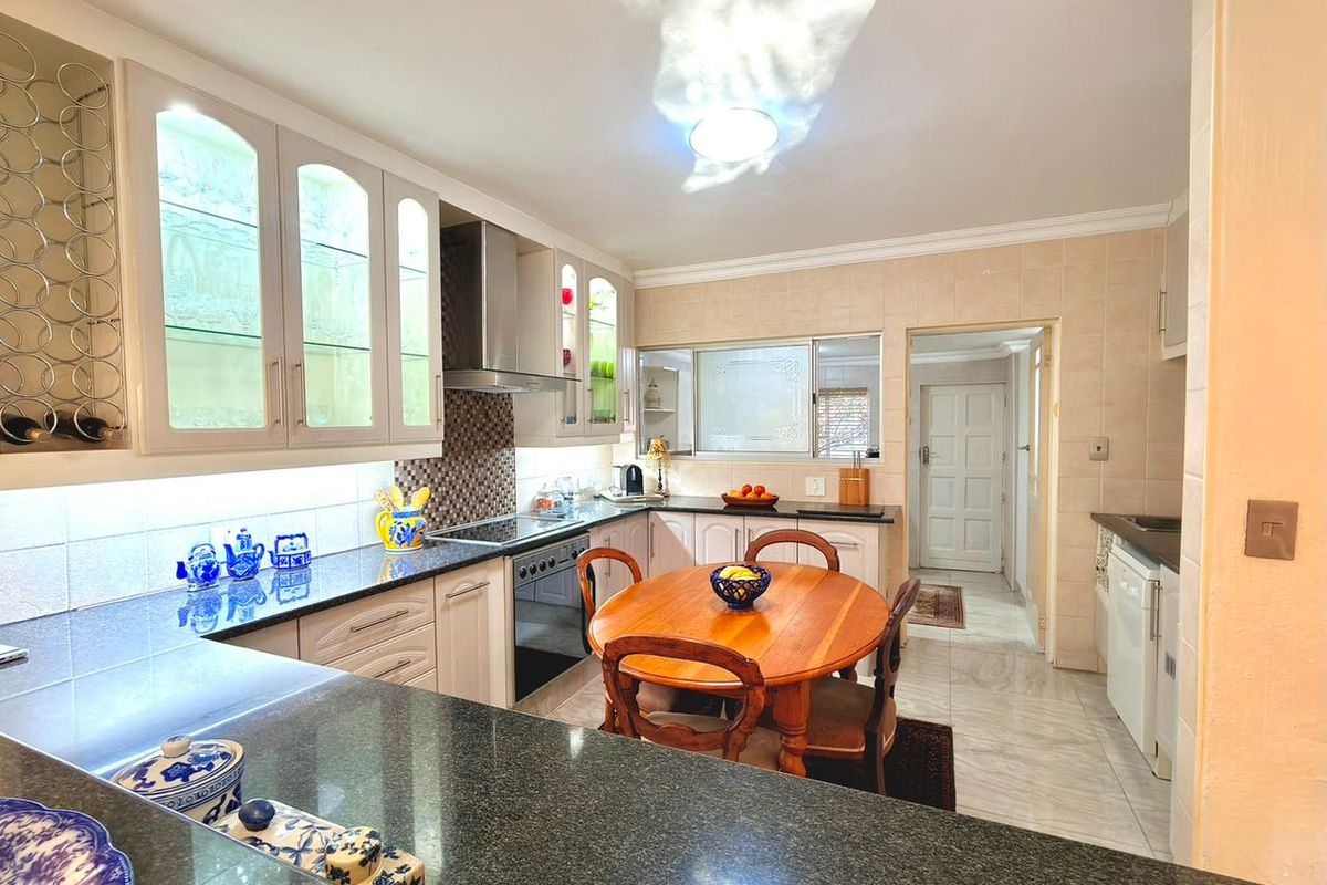 A functional kitchen featuring granite countertops, built-in cabinetry, a stainless steel extractor fan, and an integrated oven, with an adjacent dining area.