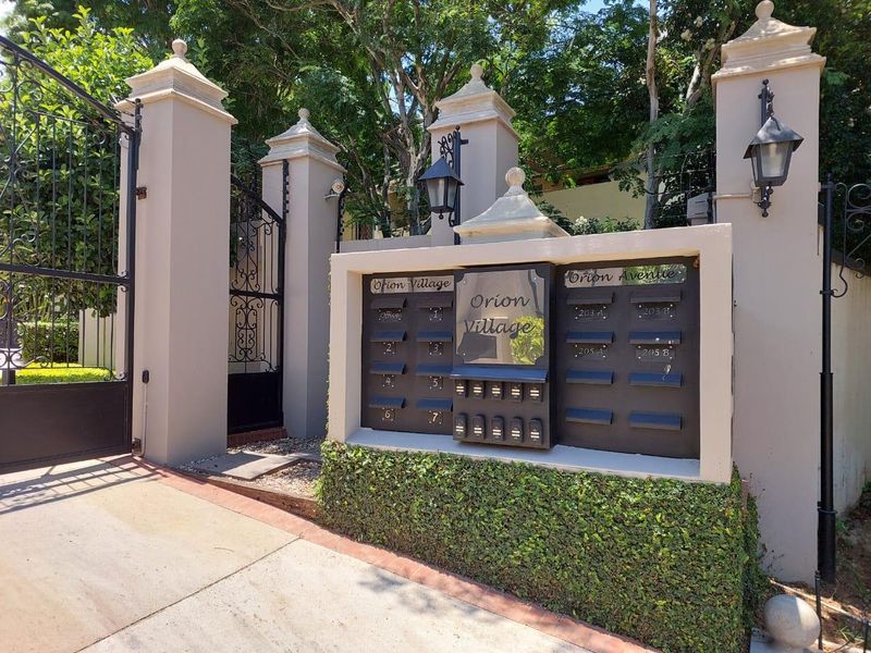 Entrance to Orion Village townhouse complex featuring secure wrought iron gates, masonry pillars, and a central communal mailbox structure.