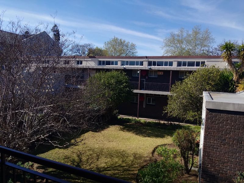 View of the rear exterior of the townhouse complex, featuring a shared garden area, brick facade, and balcony access.