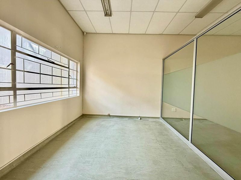 An empty office space featuring a suspended ceiling, large windows with security bars, and a modern glass partition wall.