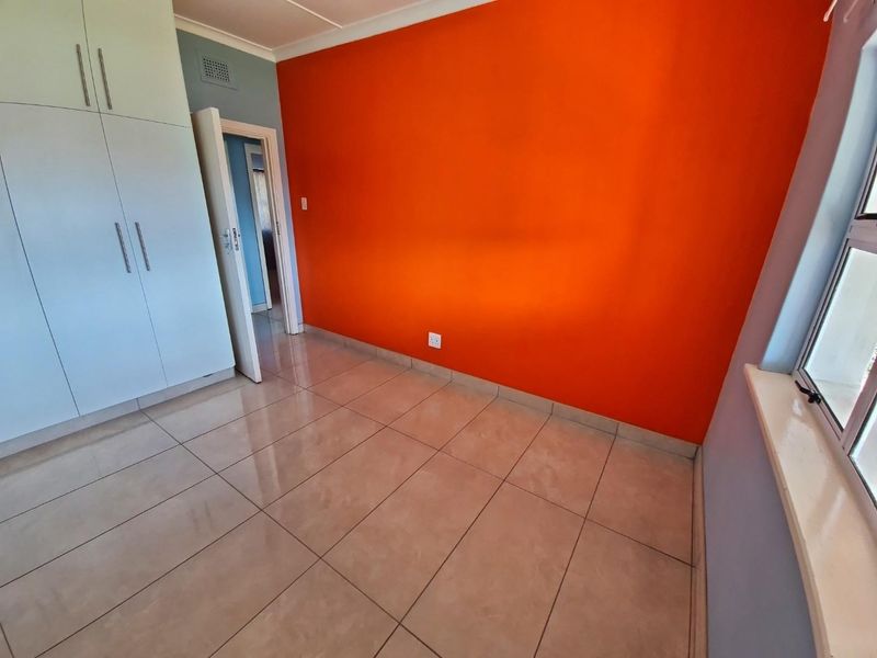 An empty bedroom featuring tiled flooring, built-in cupboards, and a vibrant orange accent wall.