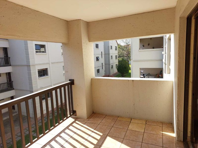 A covered balcony featuring tiled flooring and a metal balustrade, offering an open view of the surrounding apartment complex.