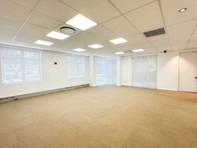 A bright, open-plan office space featuring a suspended ceiling with recessed LED lighting, carpeted flooring, and perimeter trunking for electrical and data connectivity.