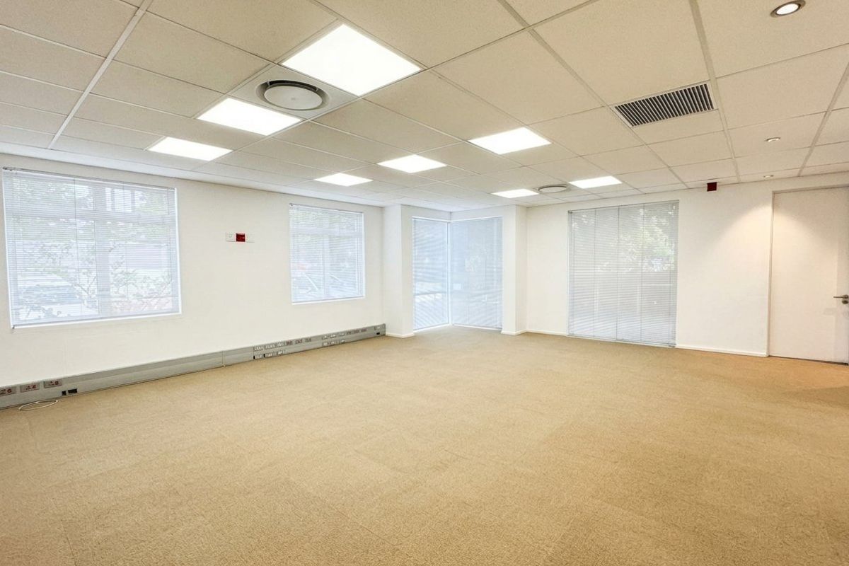 A bright, open-plan office space featuring a suspended ceiling with recessed LED lighting, carpeted flooring, and perimeter trunking for electrical and data connectivity.