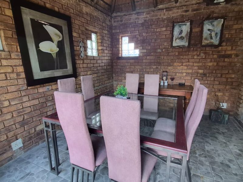 A covered patio area featuring exposed brick walls, tiled flooring, and a thatch roof, providing a rustic outdoor dining space.
