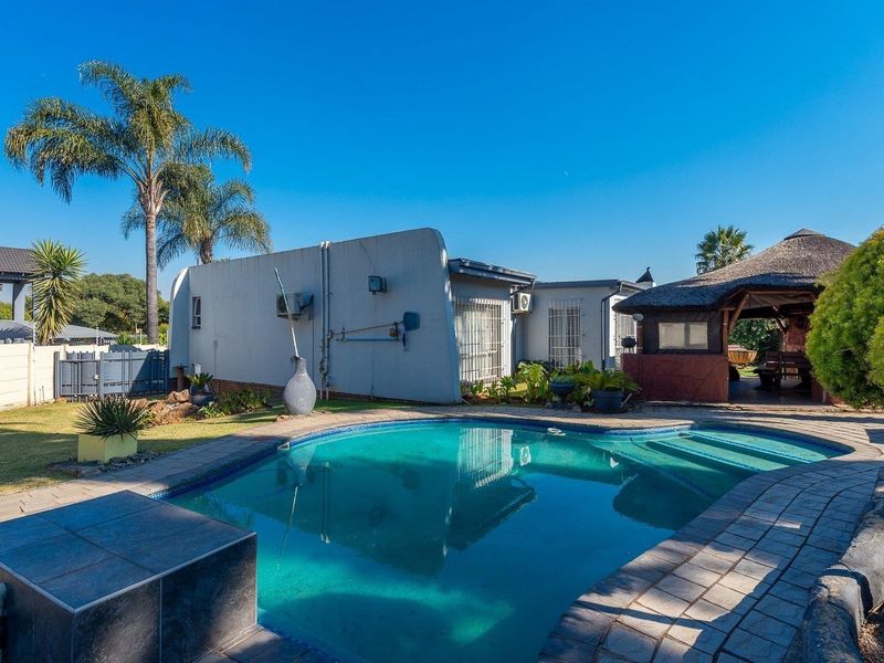Outdoor pool area featuring a swimming pool, paved surround, and a thatched lapa, set within a landscaped garden.