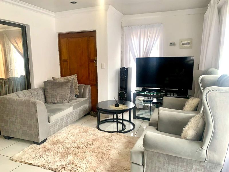 A bright living room featuring tiled flooring, cove cornicing, and recessed downlights, providing a functional and neutral space for relaxation.