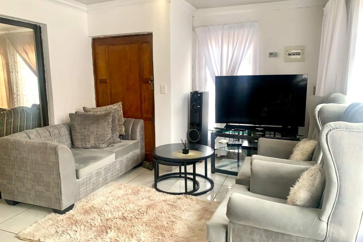 A bright living room featuring tiled flooring, cove cornicing, and recessed downlights, providing a functional and neutral space for relaxation.