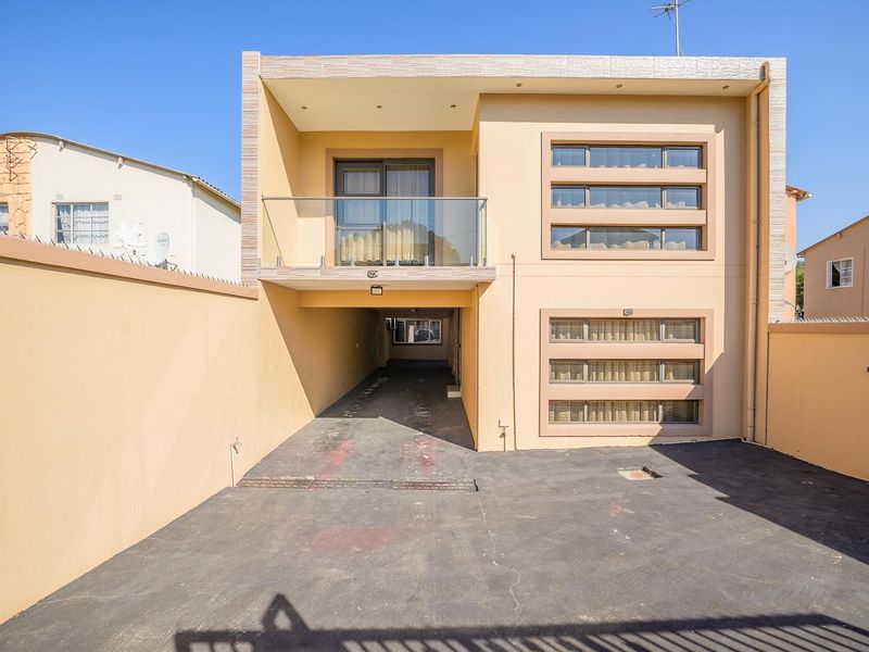 Modern two-story residential facade featuring a paved driveway, integrated balcony with glass balustrade, and contemporary horizontal window detailing.