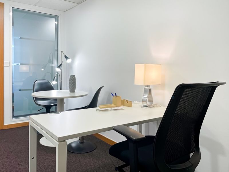 A professional office space featuring a modern desk setup, carpeted flooring, and a frosted glass partition for privacy.