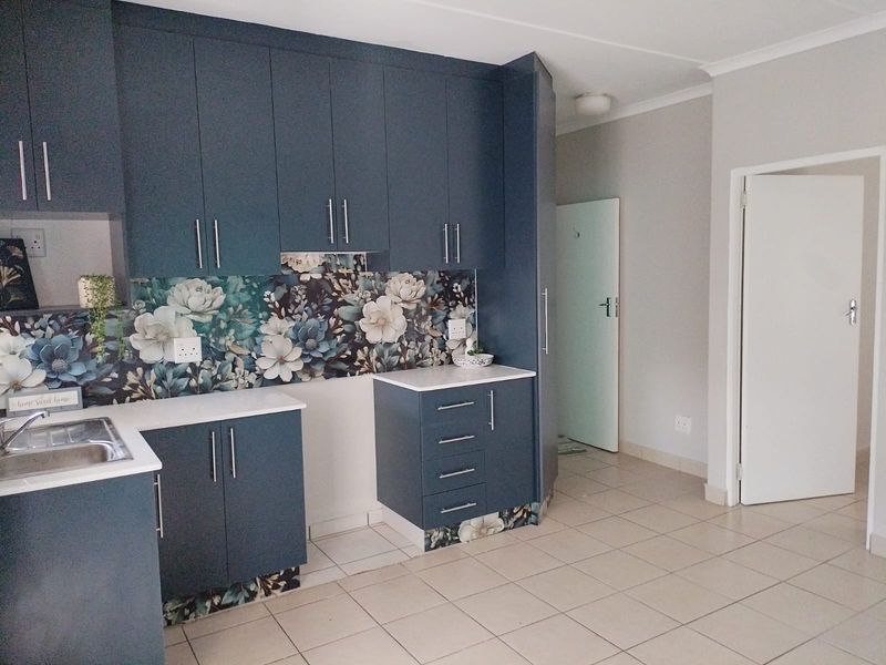 Modern kitchen featuring dark blue cabinetry, floral tiled splashback, stainless steel sink, and neutral floor tiles in a clean, well-maintained space.