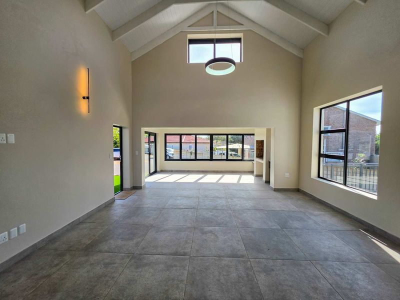 Spacious open-plan living area featuring a high vaulted ceiling with exposed rafters, large format floor tiles, and a built-in braai area.