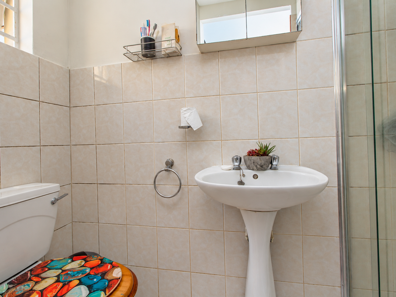 A functional bathroom featuring a pedestal basin, toilet, and a glass-enclosed shower with neutral ceramic wall tiling.
