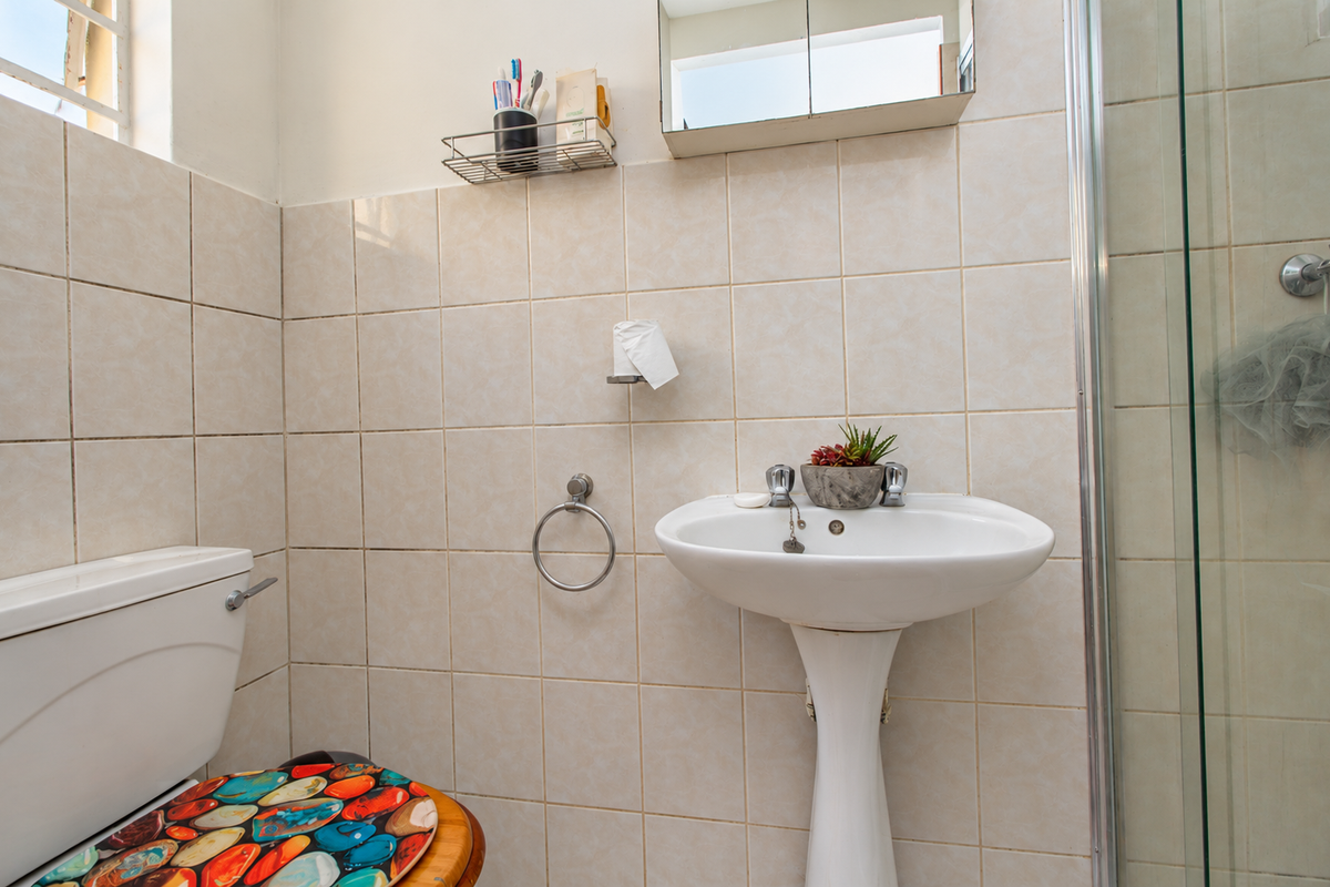A functional bathroom featuring a pedestal basin, toilet, and a glass-enclosed shower with neutral ceramic wall tiling.