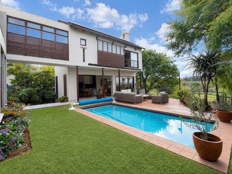 Rear exterior view featuring a swimming pool, wooden deck, and a two-story residence with balcony and patio access.