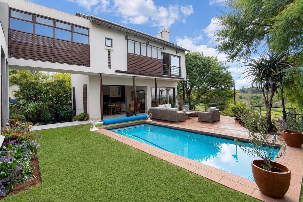 Rear exterior view featuring a swimming pool, wooden deck, and a two-story residence with balcony and patio access.