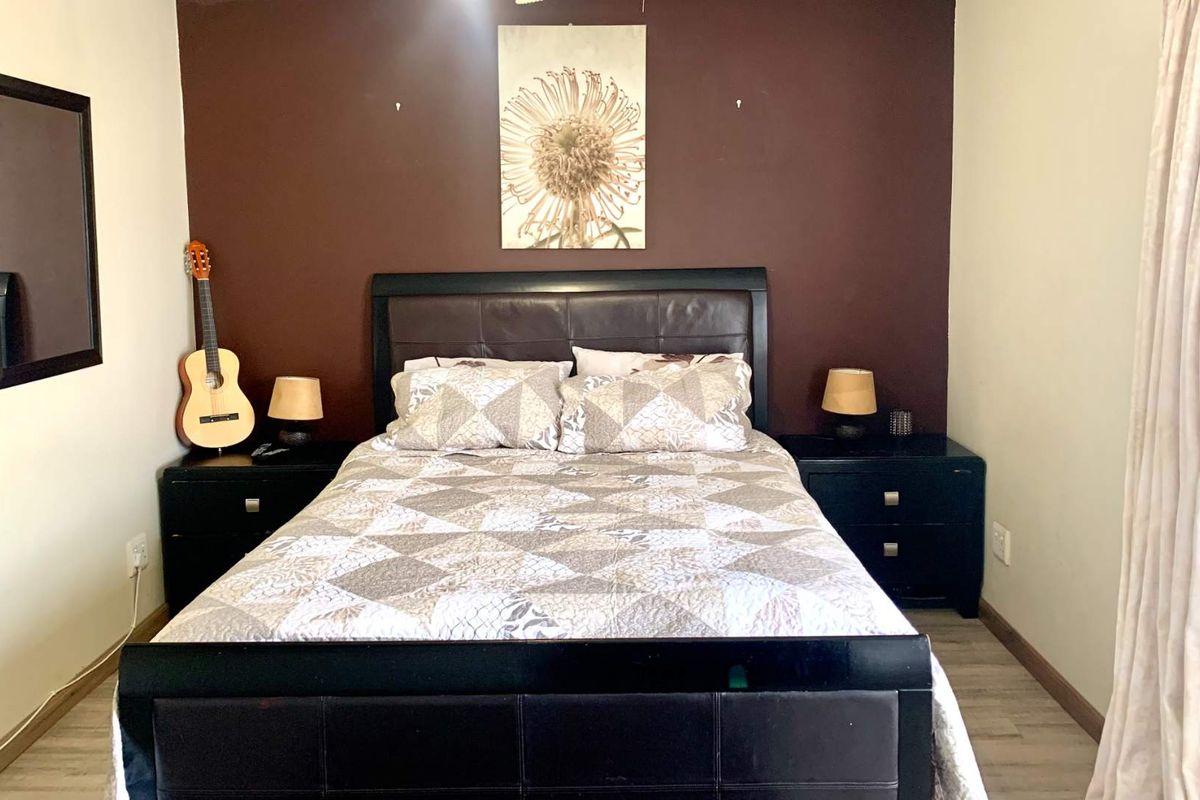 A bedroom featuring a dark accent wall, light-toned flooring, and neutral curtains.