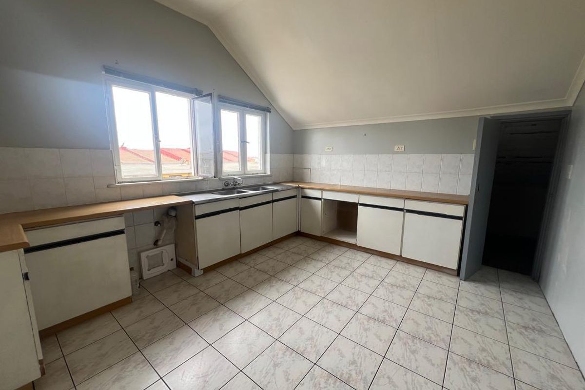 A dated kitchen area featuring tiled flooring, white cabinetry, and a double sink, set under a sloped ceiling with natural light.
