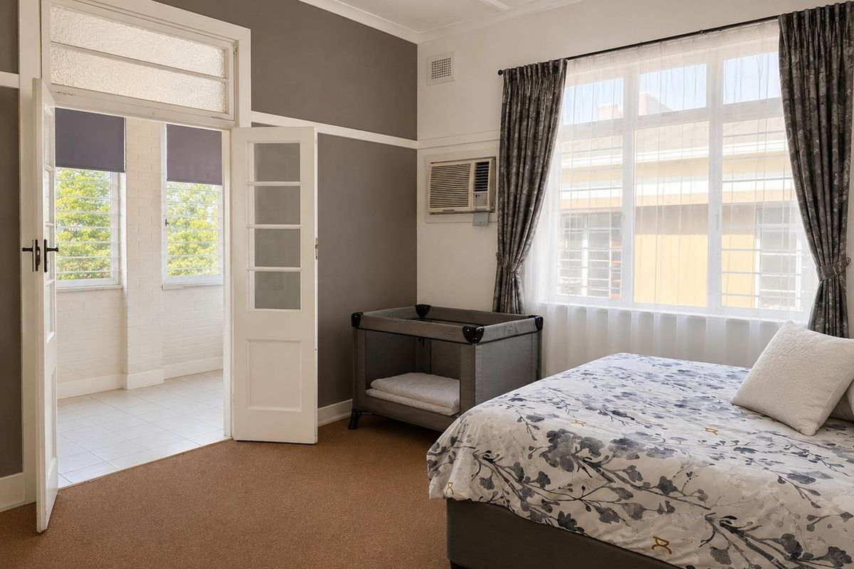 A well-lit bedroom featuring classic architectural details, including a picture rail, cornice, and french doors leading to an adjoining sunroom or balcony area.