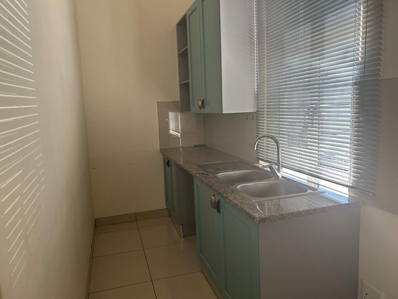 A functional scullery area featuring granite countertops, a double basin sink, and ample fitted cabinetry with a clean, modern finish.