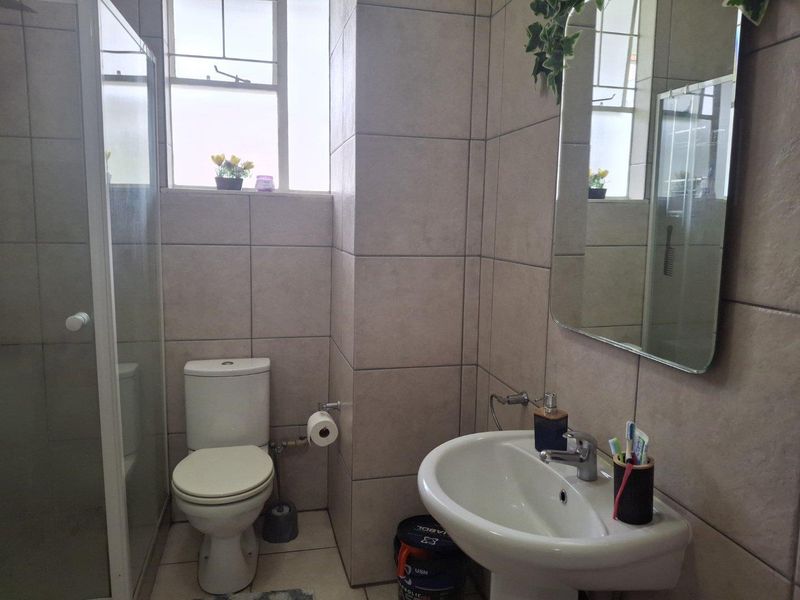 A functional bathroom featuring a pedestal basin, toilet, and a glass-enclosed shower, finished with neutral wall and floor tiling.